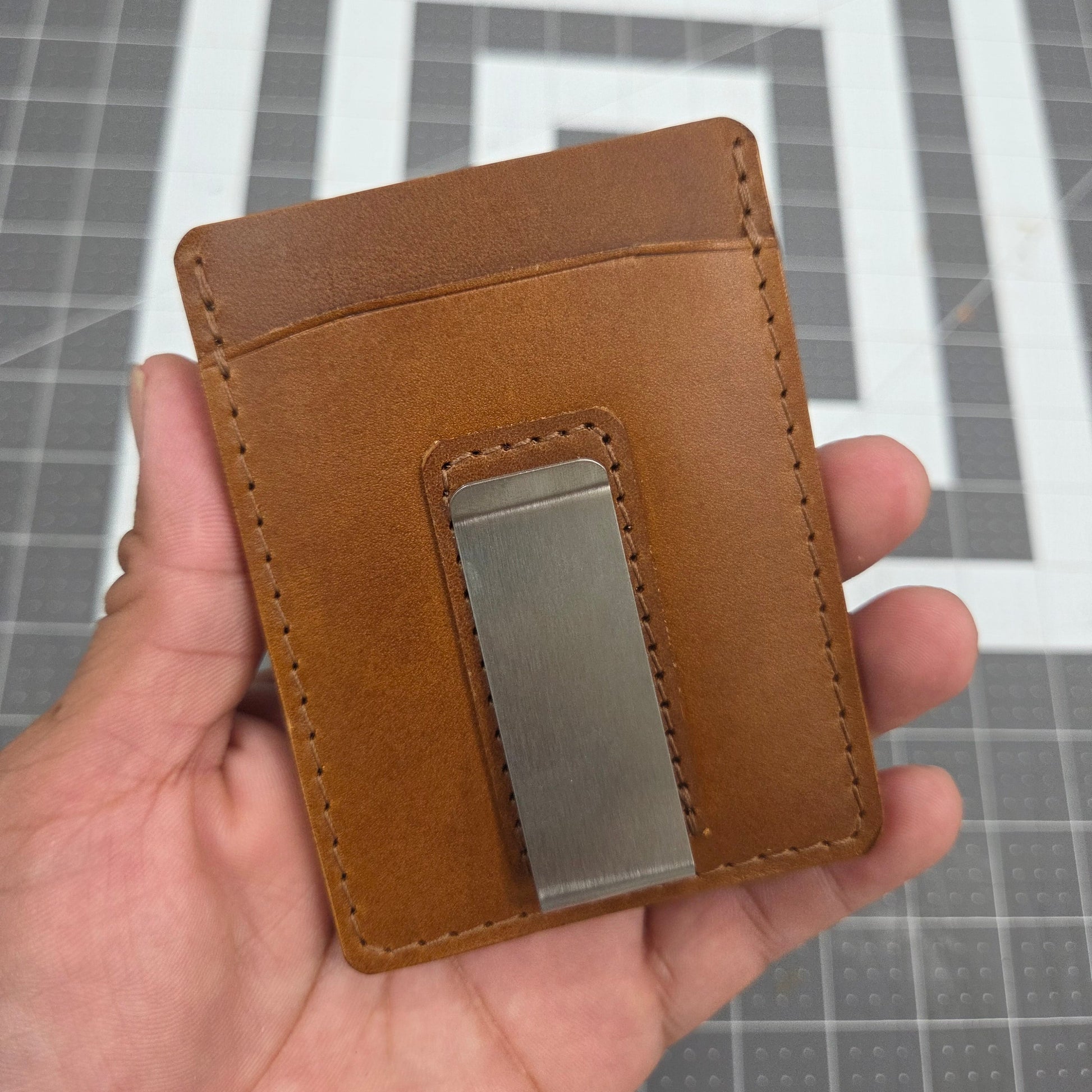 Brown leather wallet with a metal clip held in a hand against a gray grid background