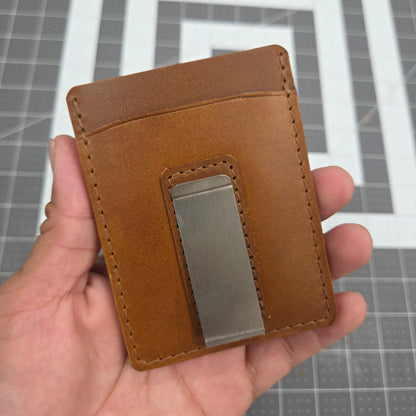 Brown leather wallet with a metal clip held in a hand against a gray grid background